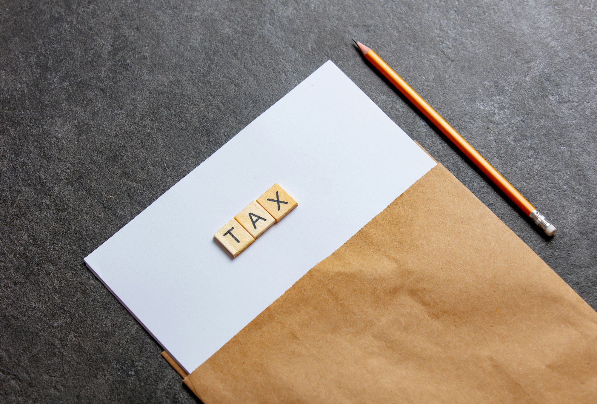 paper sheet and pencil with TAX letters on gray background